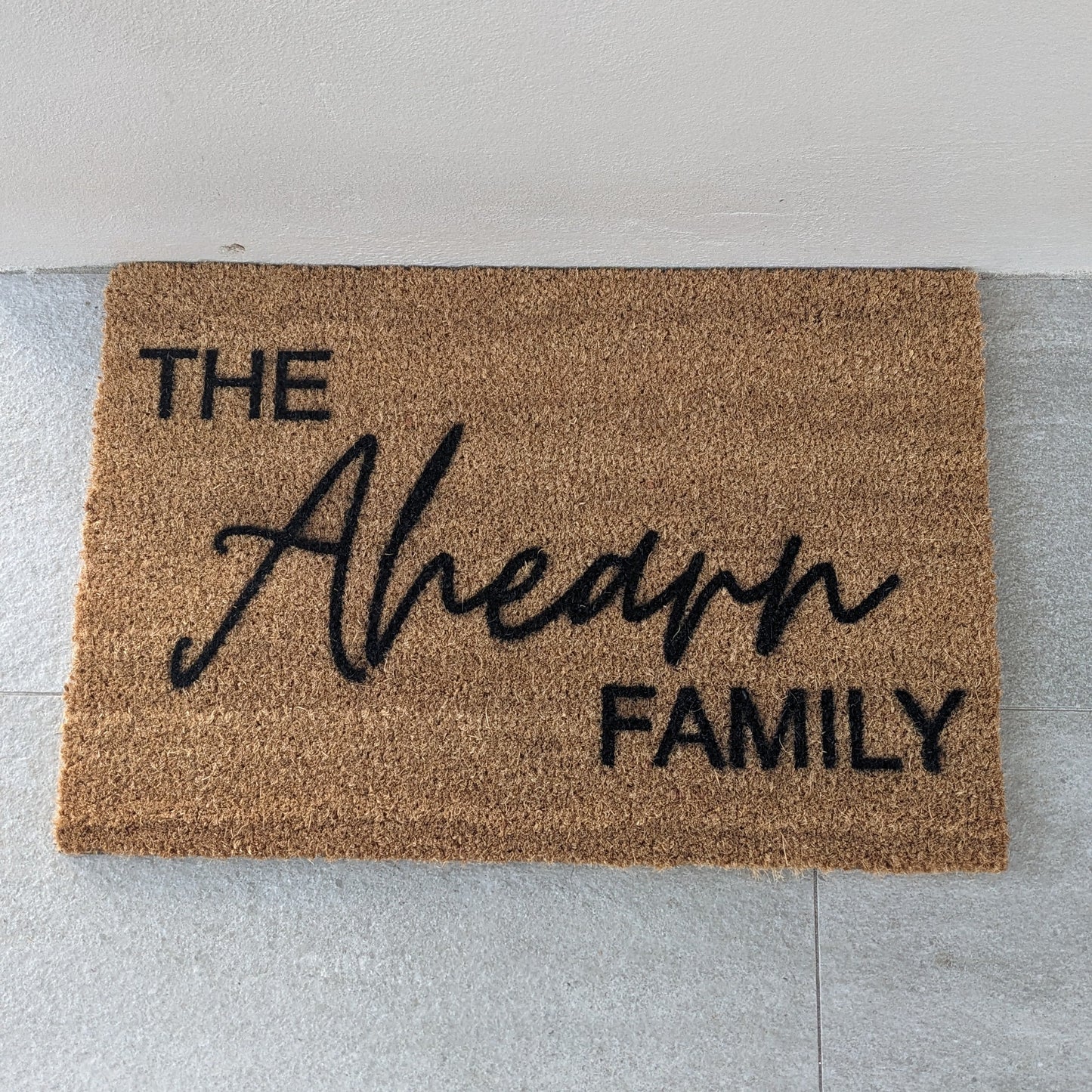 Personalised Doormat with 'The Family' text on a light gray floor.