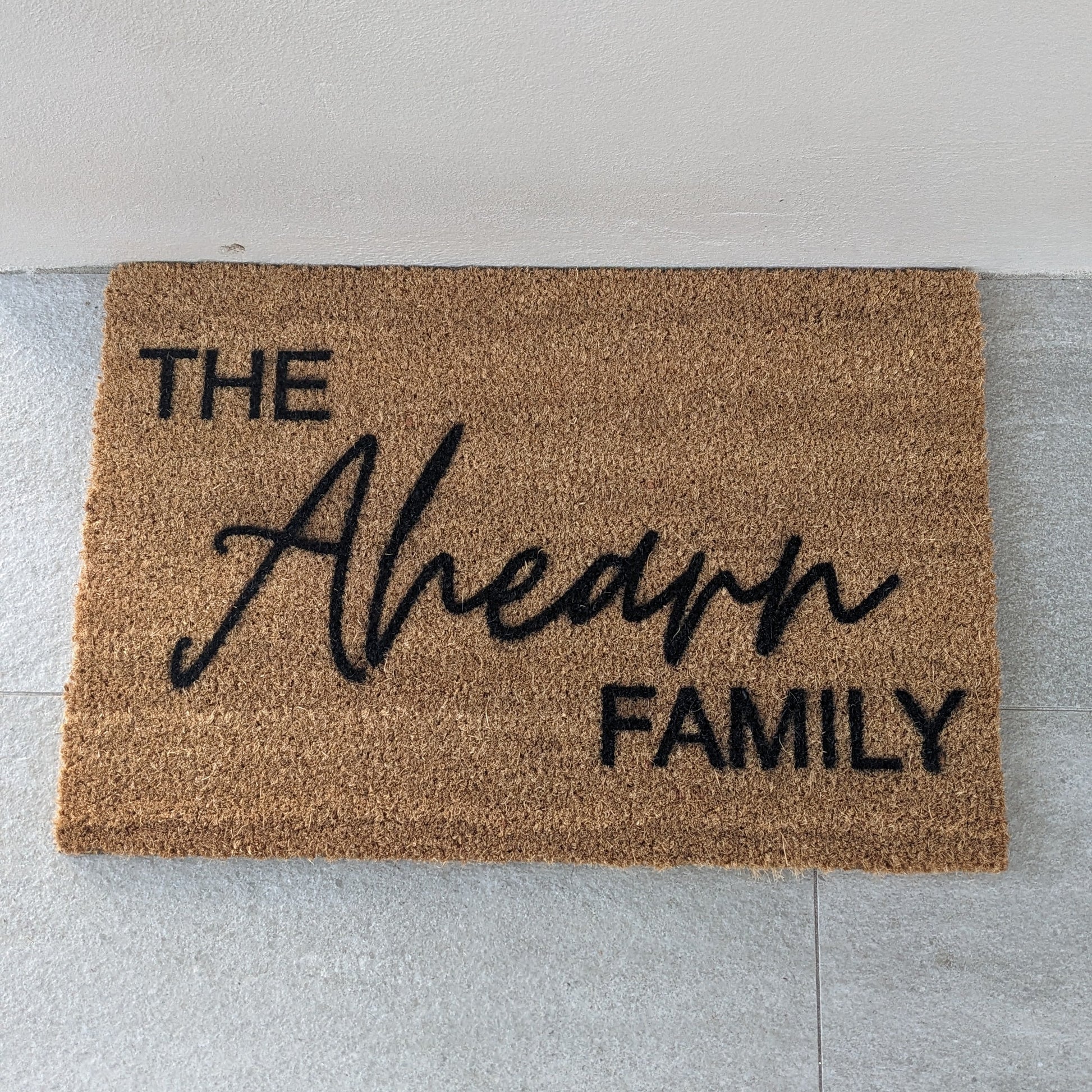 Personalised Doormat with 'The Family' text on a light gray floor.